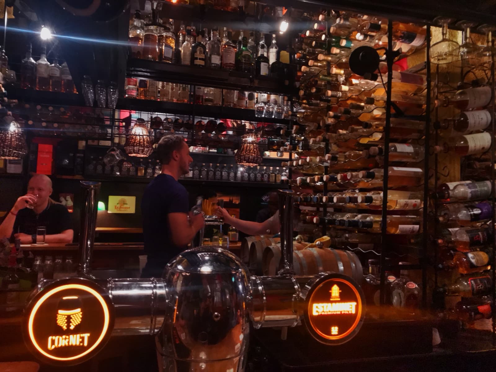 A warmly lit Amsterdam bar, bottle racks to the ceiling and beer taps glowing